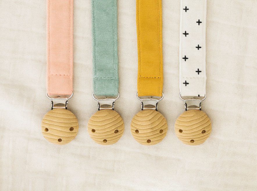 All four Willa Boo dummy catchers in pink, green, yellow and white straps on a beige background