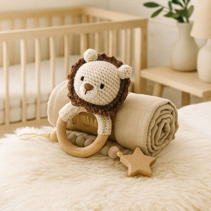 Crocheted lion toy with wooden ring and star on a blanket in a crib setting