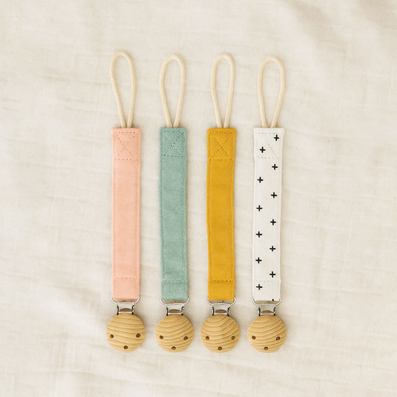 All four Willa Boo dummy catchers in pink, green, yellow and white straps on a beige background