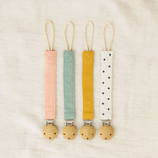 All four Willa Boo dummy catchers in pink, green, yellow and white straps on a beige background