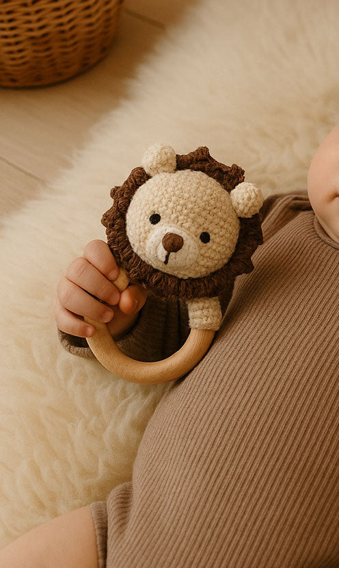 Baby holding a lion-shaped teething ring on a soft surface